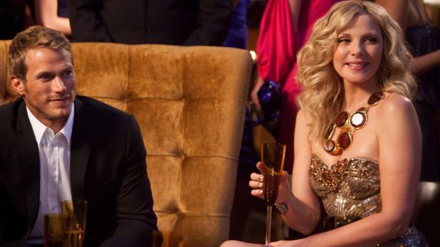Kim Cattrall und ein Mann in einem Anzug sitzen mit Champagnergläsern auf einer Party.