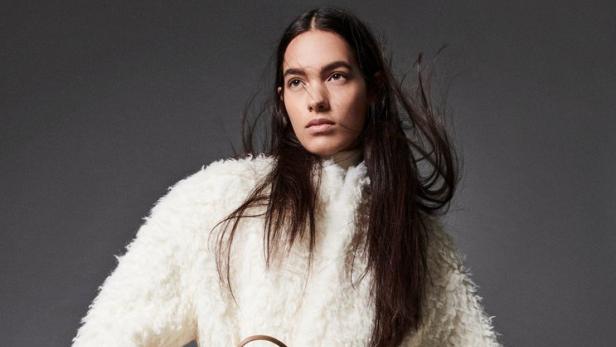 Eine Frau mit einem weißen Mantel, der mit einem braunen Gürtel gebunden ist.