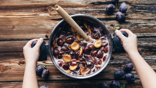 Ein Topf mit Pflaumenkompott wird auf einem Holztisch zubereitet.