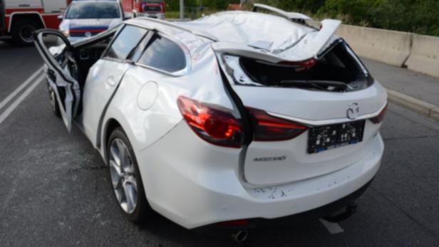 Ein weißer Mazda Kombi mit schweren Schäden am Heck und geöffneter Tür nach einem Unfall.