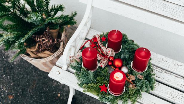 Ein Adventskranz mit vier roten Kerzen auf einer weißen Bank.