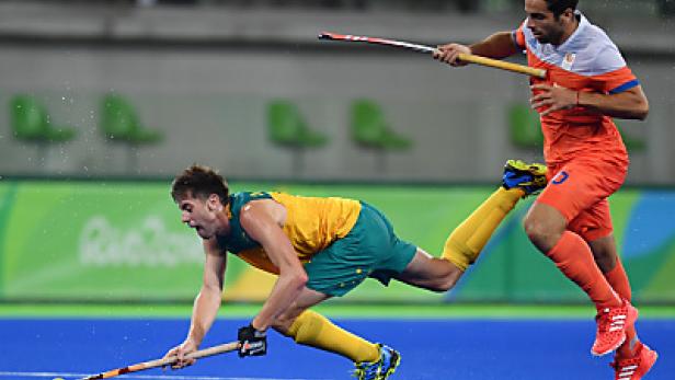 Zwei Hockeyspieler kämpfen um den Ball auf einem blauen Spielfeld.