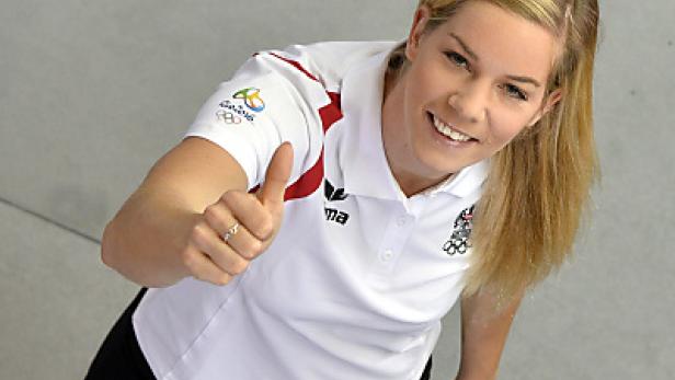 Eine lächelnde Sportlerin im österreichischen Olympia-Team-Outfit zeigt den Daumen nach oben.