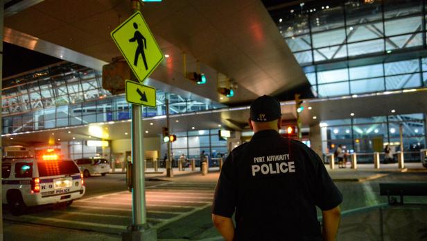 Ein Polizist der Hafenbehörde steht an einem Zebrastreifen vor einem Flughafen.