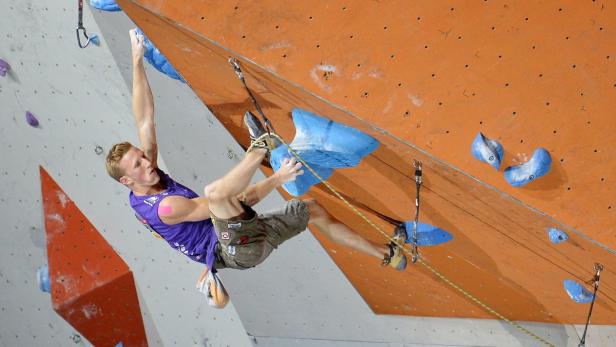Ein Mann klettert an einer Kletterwand mit bunten Griffen.