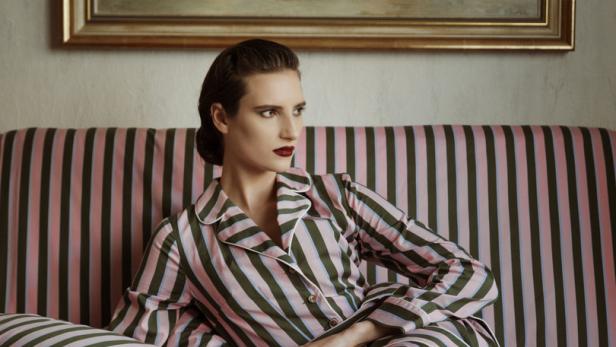 Eine Frau im gestreiften Pyjama sitzt auf einem Sofa vor einem Gemälde.