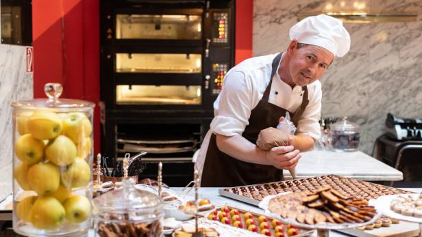 Ein Konditor verziert Gebäck mit Schokolade in einer Konditorei.