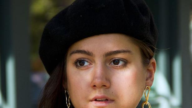 Eine Frau mit Baskenmütze und gestreiftem Oberteil trägt auffällige goldene Ohrringe.