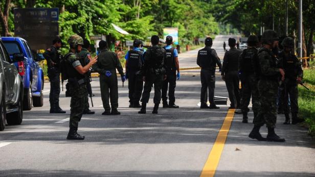 Polizei und Militär untersuchen einen Tatort auf einer abgesperrten Straße.