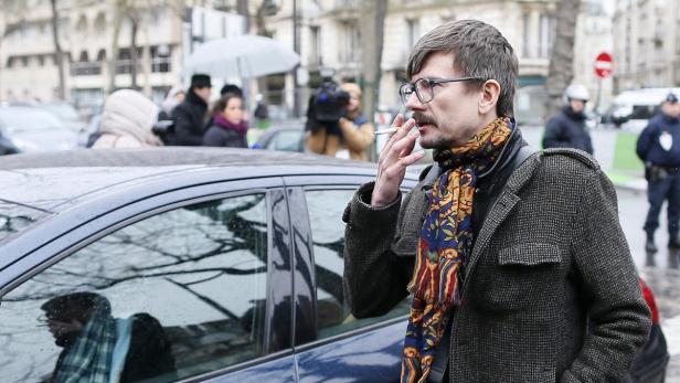 Ein Mann mit Brille und Schal raucht eine Zigarette auf der Straße.