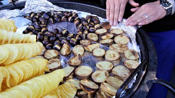 Ein Verkäufer bietet geröstete Kastanien, Kartoffelchips und Bratkartoffeln an.