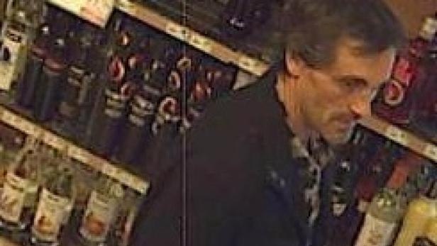 Ein Mann steht vor einem Regal mit alkoholischen Getränken.