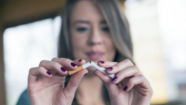 Eine Frau zerbricht eine Zigarette in zwei Hälften.