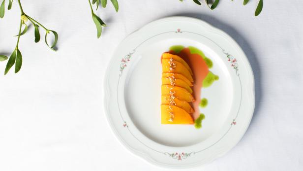 Ein Teller mit geschnittenen Mangos, garniert mit Sesam und grüner Soße, umgeben von Mistelzweigen.