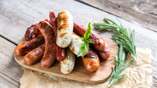 Verschiedene gegrillte Würste liegen auf einem Holzbrett mit Kräutern.