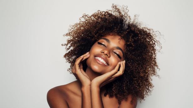 Eine Frau mit lockigem Haar lächelt mit geschlossenen Augen.