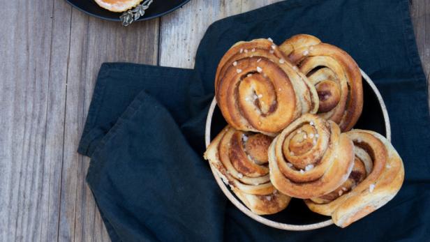 Zimtschnecken auf einem Teller und in einer Schale auf einem Holztisch.