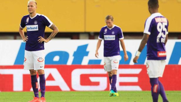 Drei Fußballspieler in lila-weißen Trikots stehen auf dem Rasen.