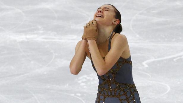 Eine weinende Eiskunstläuferin mit Handschuhen auf dem Eis.