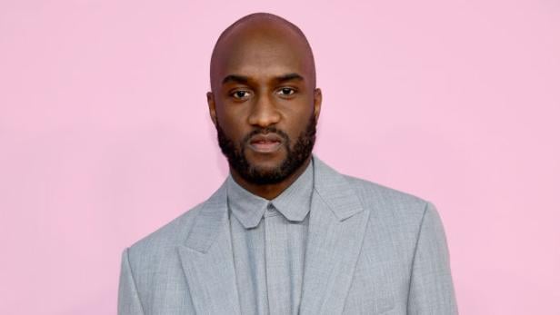 Virgil Abloh trägt einen grauen Anzug vor einem rosa Hintergrund.