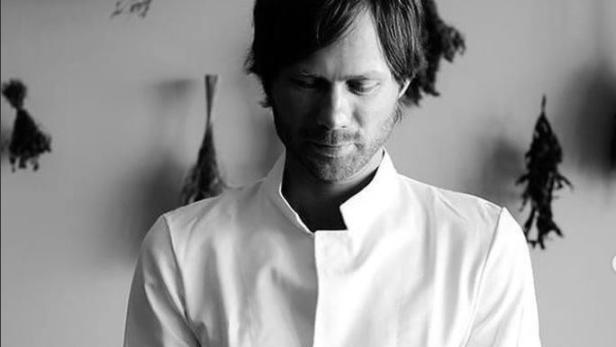 Ein Mann in Kochkleidung hält eine Schale mit Kräutern in den Händen.