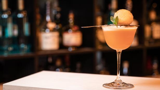 Ein Cocktail in einem eleganten Glas, garniert mit einer Melonenkugel und Minze.