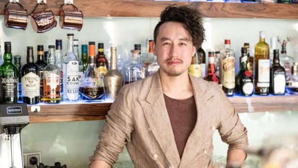 Ein Barkeeper steht vor einem Regal mit verschiedenen Spirituosenflaschen.