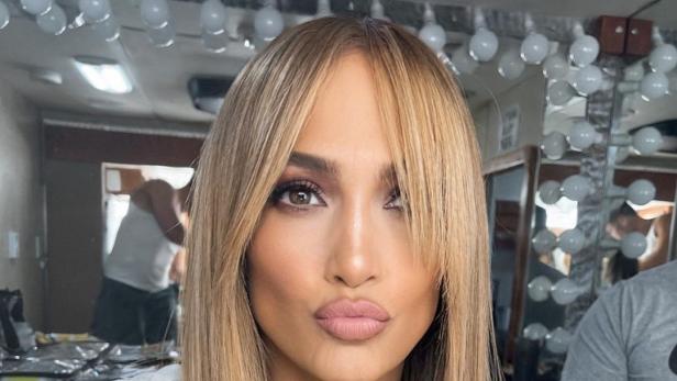 Jennifer Lopez posiert mit blonden Haaren und Pony für ein Foto.