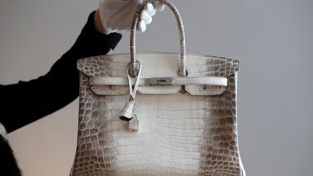 Eine weiße Hermès Birkin Bag aus Krokodilleder wird von einer Person mit weißen Handschuhen gehalten.