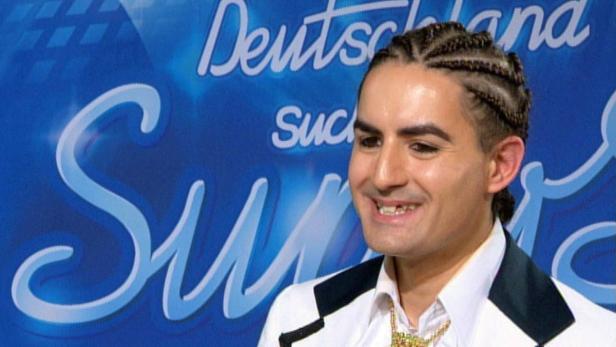 Ein Mann mit Zöpfen lächelt vor dem „Deutschland sucht den Superstar“-Logo.