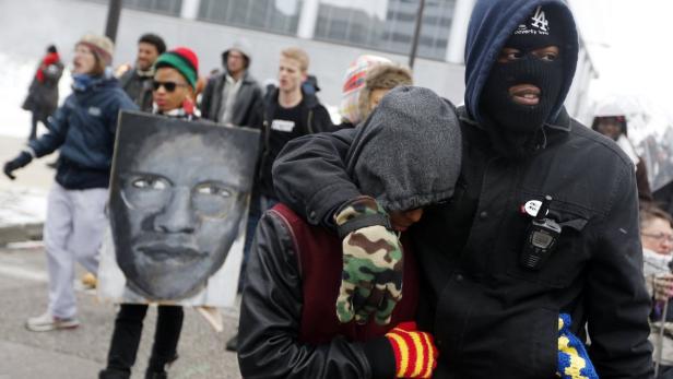 Demonstranten marschieren mit einem Porträt von Malcolm X und unterstützen sich gegenseitig.