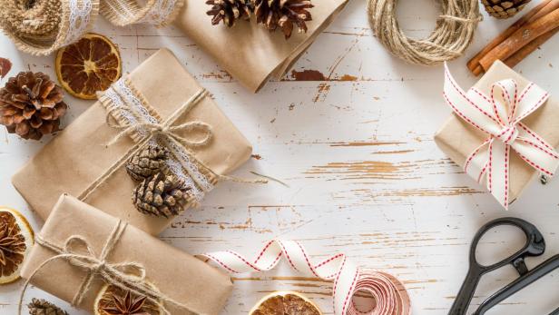 Geschenke, Tannenzapfen, getrocknete Orangenscheiben und Bänder auf einem Tisch.