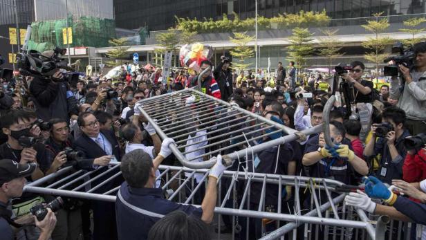 Eine Menschenmenge drängt sich vor einer Absperrung, während Fotografen die Szene dokumentieren.