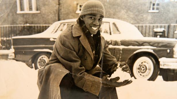 Ein lächelnder Mann sitzt im Schnee vor einem Oldtimer.