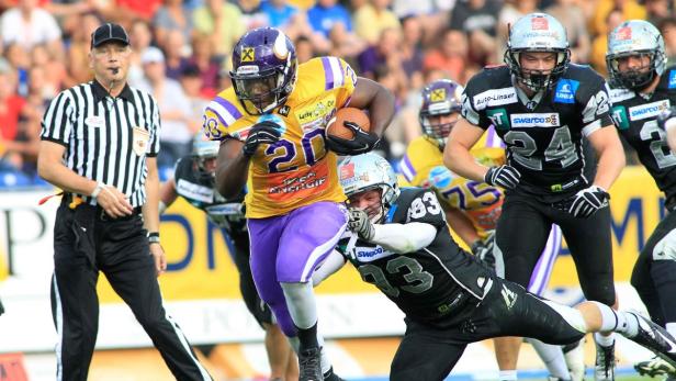 Ein American-Football-Spieler mit Ball wird von einem Gegenspieler angegangen.