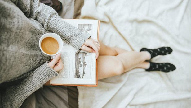 Ein Buch, eine Tasse Kaffee - auf dem Schoß einer Frau