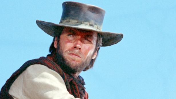 Clint Eastwood mit Bart und Cowboyhut vor blauem Himmel.