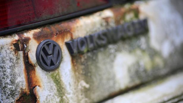 Das VW-Logo und der Schriftzug „Volkswagen“ sind an einem verrosteten Auto zu sehen.