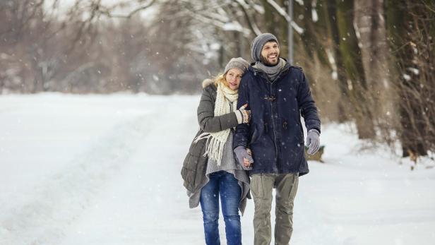 Ein Paar spaziert Hand in Hand durch eine verschneite Winterlandschaft.