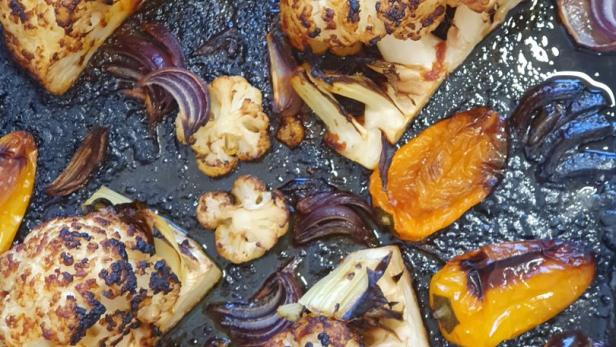 Gebratener Blumenkohl mit gelben Paprika und roten Zwiebeln auf einem Backblech.