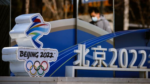 A man is reflected in a mirror as he walks past the logo of the Beijing 2022 Olympics in Beijing