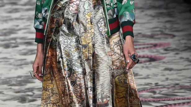 Ein Model präsentiert ein Outfit mit einer Karte bedruckten Rock und einer grünen Jacke mit Blumenmuster.