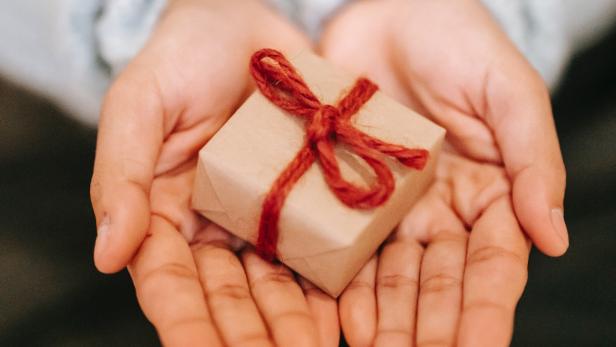 Ein kleines Geschenk mit roter Schleife liegt in den Händen einer Person.