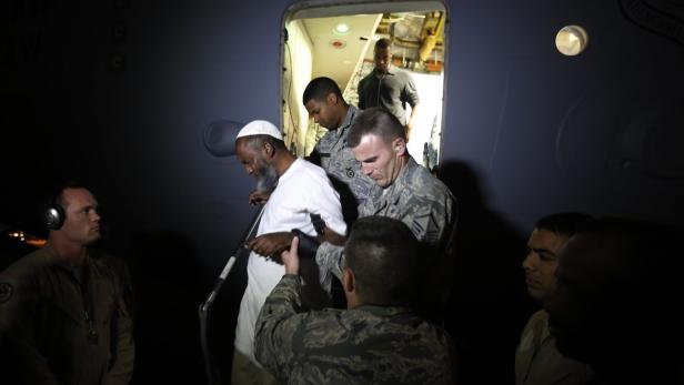 Ein älterer Mann mit Bart und Gebetsmütze wird von US-Soldaten aus einem Flugzeug begleitet.