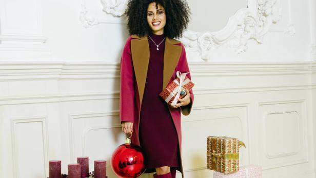 Eine Frau mit Afro hält Weihnachtsgeschenke in einem festlich geschmückten Raum.