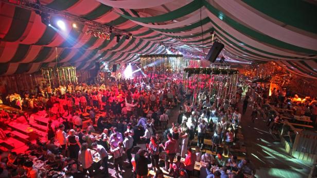 Ein volles Bierzelt mit Menschen an Tischen und auf Bänken unter einer dekorierten Decke.