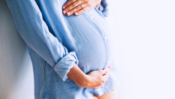 Pregnant woman holds hands on belly at home interiors.