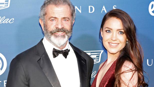 Mel Gibson posiert mit einer jungen Frau auf einer Veranstaltung.