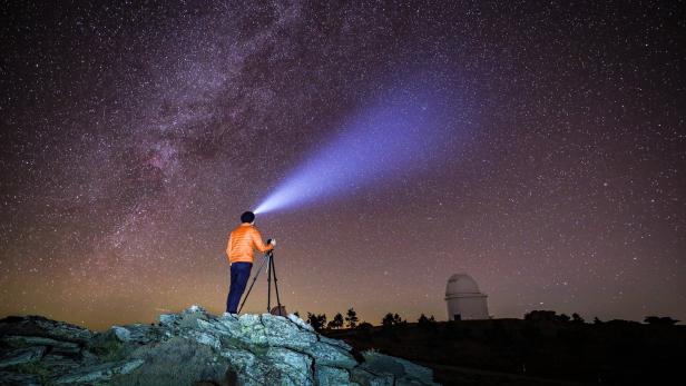 Ein Mann fotografiert mit Stativ und Stirnlampe den Sternenhimmel.