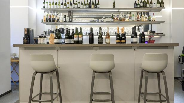 Eine Bar mit drei Hockern und Regalen voller Flaschen.